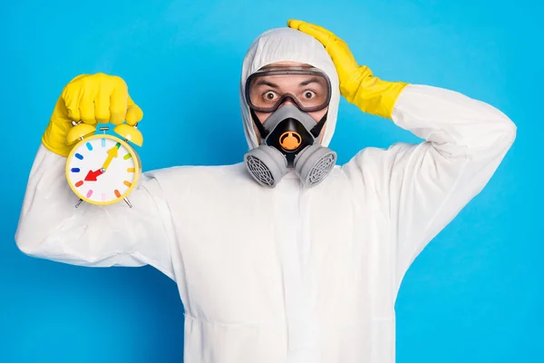 Portrait of amazed man hold clock impressed fast speed time ncov spread touch yellow latex gloves head wear white suit goggles isolated over blue color background — Stock Photo, Image