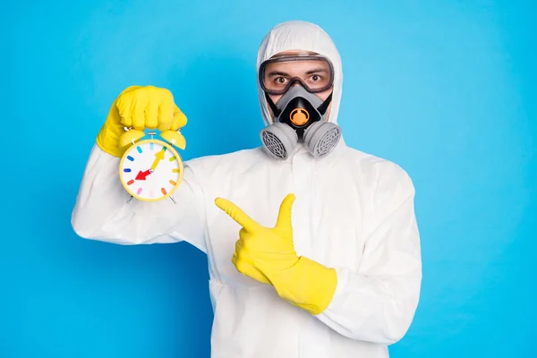 Портрет медичного працівника чоловік тримає індекс годинникової точки пальця носіння дихальної маски жовті латексні рукавички окуляри білий небезпечний костюм ізольований на синьому кольорі — стокове фото
