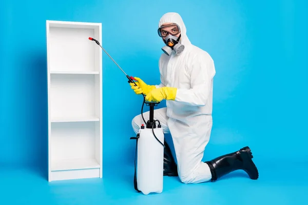 Foto completa del corpo dell'uomo indossare tuta hazmat bio maschera respiratoria utilizzare attrezzature spruzzatore disinfettare scaffali infezione ncov isolato su sfondo di colore blu — Foto Stock