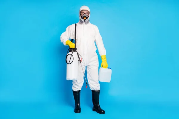 Foto de cuerpo entero del trabajador médico sostiene plástico envase productos químicos equipo pulverizador superficie de lavado ncov desgaste hazmat látex bota máscara de gas aislado color azul fondo — Foto de Stock