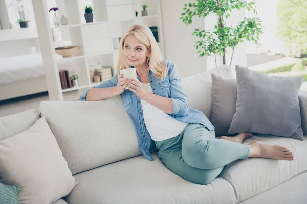 Foto van aantrekkelijke oudere volwassen huiselijke dame zitten comfortabele sofa bank drinken koffie vredig goed humeur ontspannen genieten verblijf thuis quarantaine tijd weekend woonkamer binnen — Stockfoto