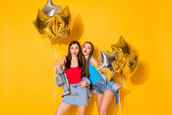 Portrait of nice attractive lovable lovely charming cheerful cheery girls holding in hands helium balls sending air kiss posing isolated on bright vivid shine vibrant yellow color background — Stock Photo, Image