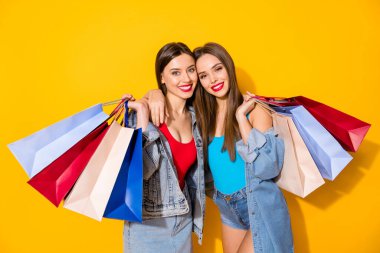 Portrait of nice attractive pretty charming perfect glamorous cheerful girls carrying colorful bags spending free time isolated on bright vivid shine vibrant yellow color background clipart