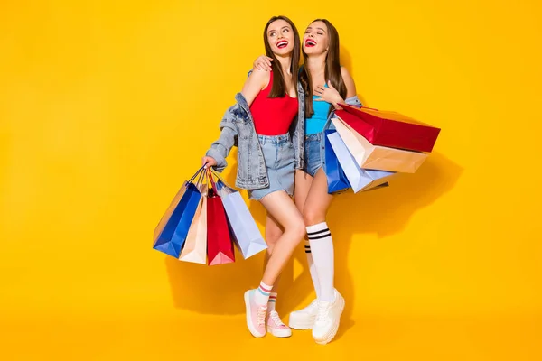 Full length body size view of nice attractive lovely pretty glad cheerful cheery brown-haired girls carrying new things clothes bargain isolated on bright vivid shine vibrant yellow color background — Stock Photo, Image