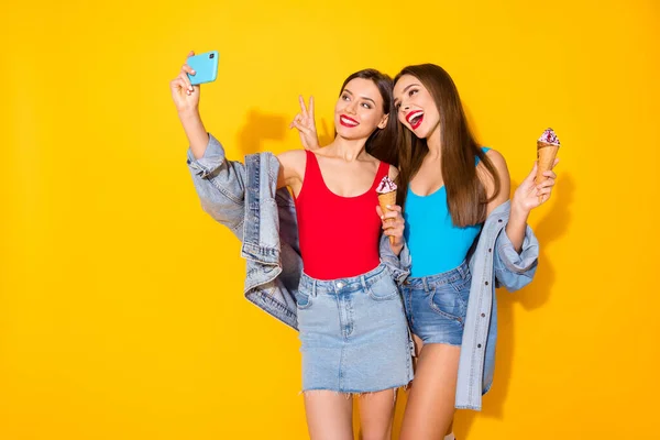 Позитивные два человека молодежь сестры блоггеры наслаждаются летняя поездка сделать селфи смартфон провести вкусный вкусный мороженое сделать V-знак носить красный синий синглет джинса изолированный яркий цвет фона — стоковое фото