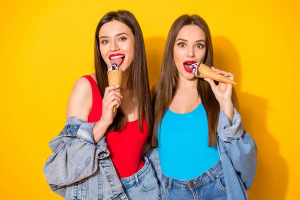 Portret van positieve vrolijke charmante meisjes jongeren eten heerlijke ijscream scoops wafel kegel dragen helder rood singlet geïsoleerd over glans kleur achtergrond — Stockfoto