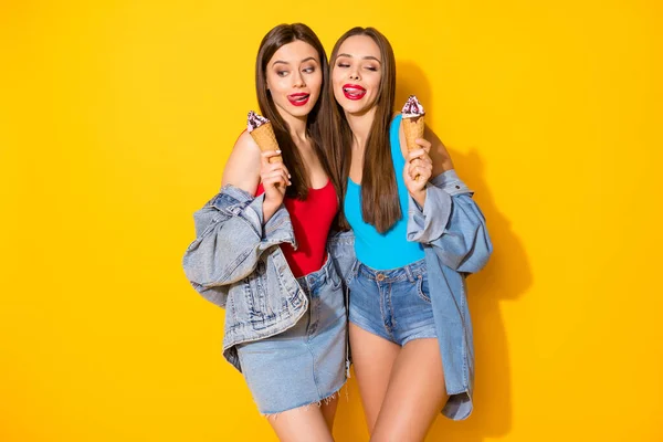 Portrait de filles gaies positives compagnons tiennent savoureux lèvres lécher la crème glacée veulent manger aussi vite que possible porter un jean rouge bleu singulet isolé fond de couleur vive — Photo