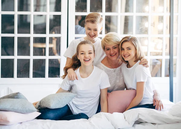 Aile anne ile oğlu ve iki kızı var eğlenceli bir pencerede beyaz t-shirt yakınındaki bir yatakta oturuyor. Yumuşak odak