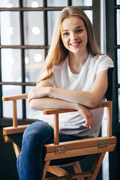 Bir pencere yakın bir sandalyede oturan beyaz t-shirt genç güzel kız portresi. Kopya alanı