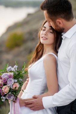 Yeni evlilik güzel çift, gelin ve damat, düğün buket nehir ve dağ ile ayakta. Yakın çekim