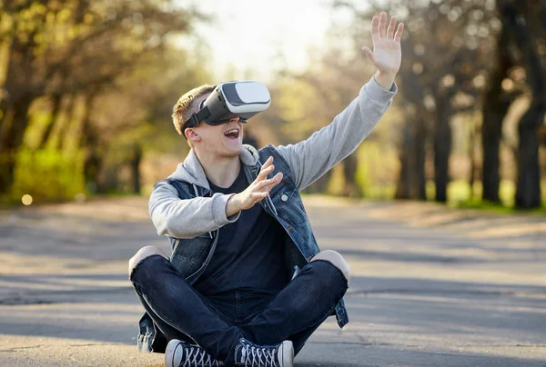 Vr ile yolda oturan genç sarışın adam gözlük ve eğlenin. Açık. Kopya alanı.