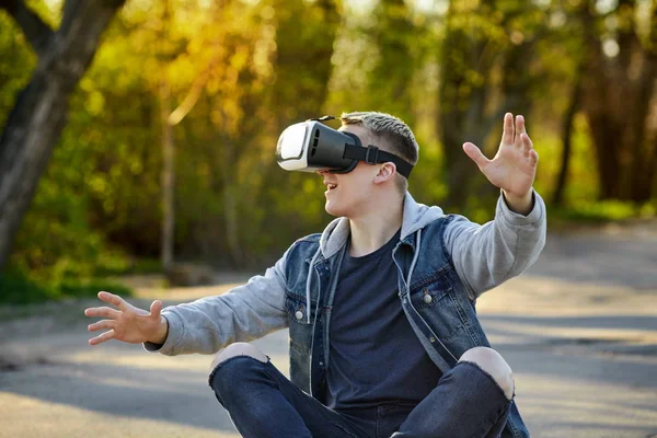 Vr ile yolda oturan genç sarışın adam gözlük ve eğlenin. Açık. Kopya alanı.