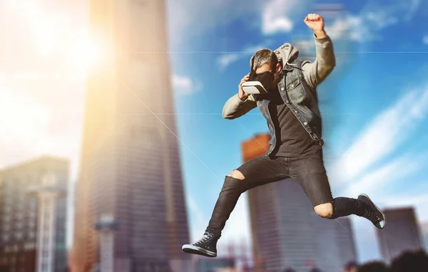 Yaratıcı kolaj. Gerçeklik bulanık satır. Genç adam bir kukuleta ile atlama ve parkour şehrin arka planda bir biulding ile yapıyor sanal gerçeklik gözlük ile ceketli. Yumuşak odak