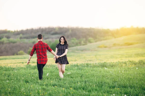 Beautiful couple holding their hands walking at the green bloomi — Stock Photo, Image