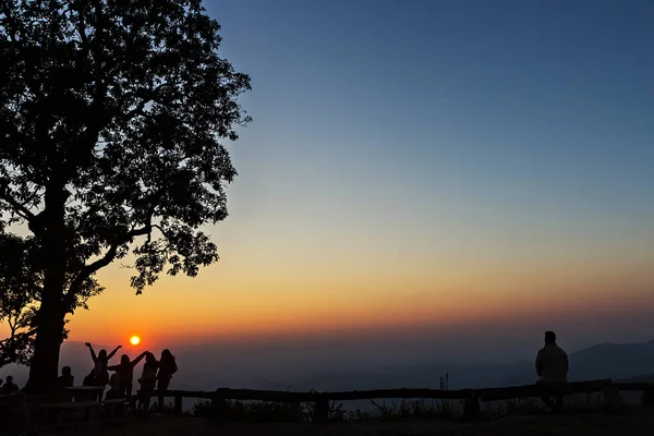 Kansat ja puut siluetoituna upealla auringonlaskulla — kuvapankkivalokuva