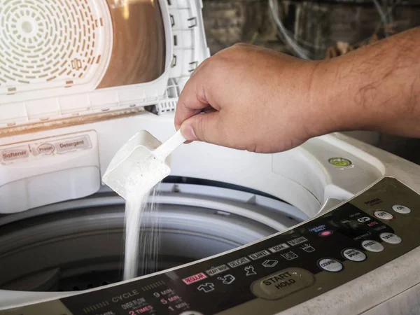 A man pouring laundry detergent or washing powder into the washing machine.