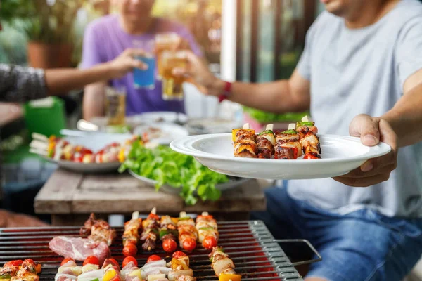 Arkadaşlar arasındaki partide elinde barbekü tabağı olan bir adam. Yiyecek, insan ve aile zaman kavramı.