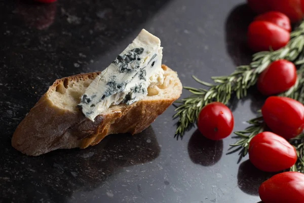 Blue cheese with french baguette, tomato and herbs on black marble table. Traditional snacks in France and Italy — Stock Photo, Image