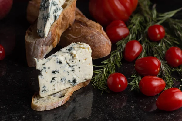 Blue cheese with french baguette, tomato and herbs on black marble table. Traditional snacks in France and Italy — Stock Photo, Image