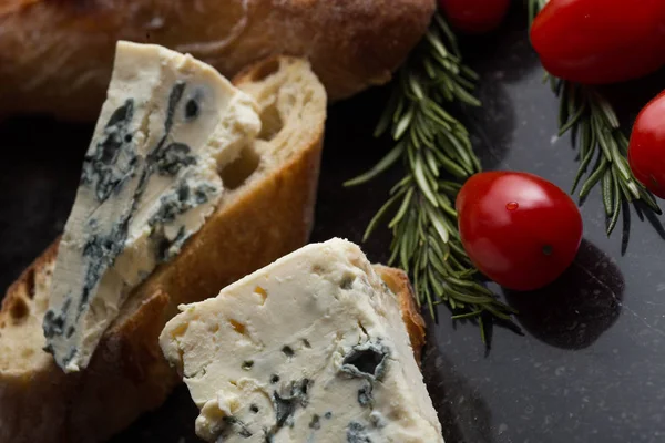 Blue cheese with french baguette, tomato and herbs on black marble table. Traditional snacks in France and Italy — Stock Photo, Image