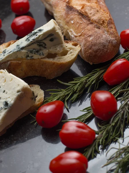 Blue cheese with french baguette, tomato and herbs on black marble table. Traditional snacks in France and Italy — Stock Photo, Image