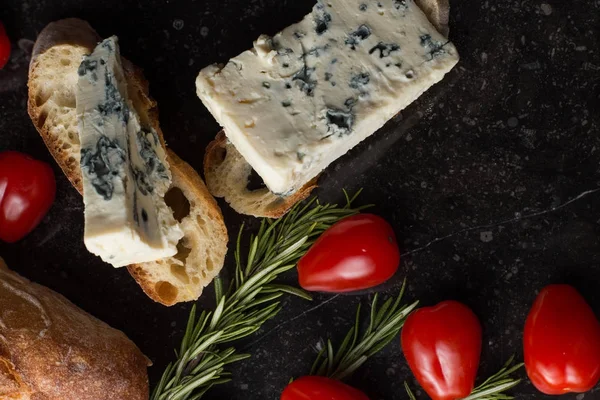 Blue cheese with french baguette, tomato and herbs on black marble table. Traditional snacks in France and Italy — Stock Photo, Image