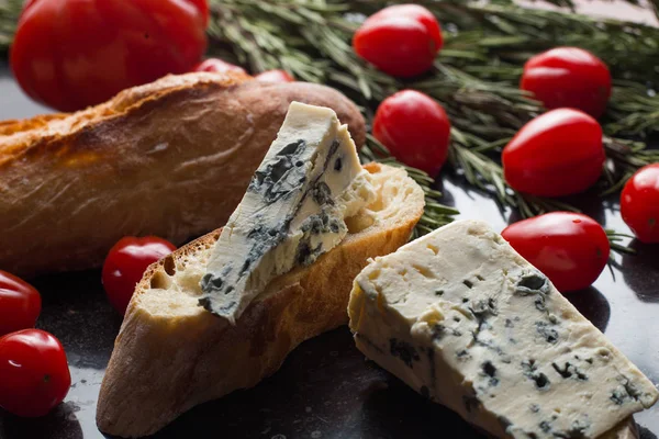 Mavi peynir ile Fransız baget, domates ve siyah mermer masa üzerinde otlar. Fransa ve İtalya geleneksel aperatifler