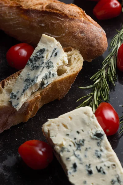 Blue cheese with french baguette, tomato and herbs on black marble table. Traditional snacks in France and Italy