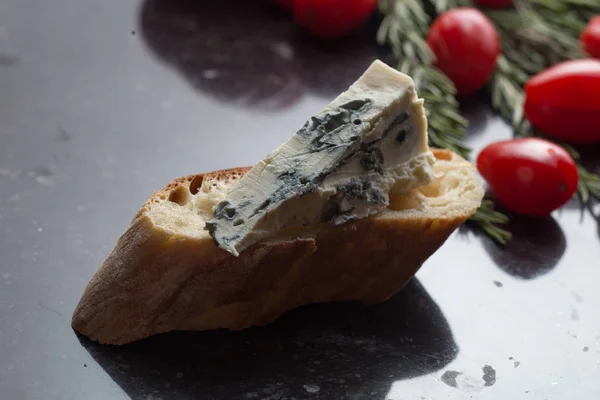 Mavi peynir ile Fransız baget, domates ve siyah mermer masa üzerinde otlar. Fransa ve İtalya geleneksel aperatifler — Stok fotoğraf