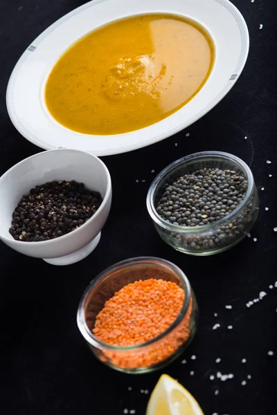 Cream soup of assorted lentil. Yellow and green lens, spices as raw for meal and lemon on black backgraund. Healthy, appetizing, delicious, vegetarian food. Top view, copy space — Stock Photo, Image