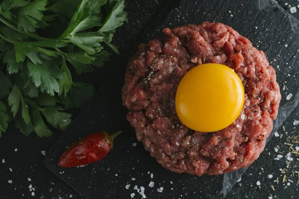 Çiğ biftek. Sığır eti çiğ et baharat, ot ve yumurta sarısı ile kıyılmış. Taze, baharatlı, lezzetli, gurme yemek ile kopya alanı, koyu arka plan üzerinde yakın çekim. Üstten Görünüm.