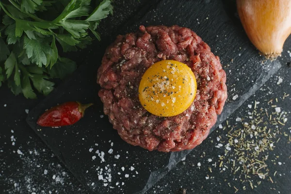 Çiğ biftek. Sığır eti çiğ et baharat, ot ve yumurta sarısı ile kıyılmış. Taze, baharatlı, lezzetli, gurme yemek ile kopya alanı, koyu arka plan üzerinde yakın çekim. Üstten Görünüm.