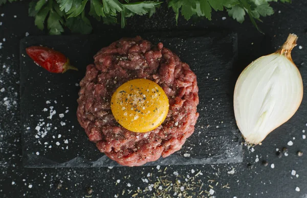 Çiğ biftek. Sığır eti çiğ et baharat, ot ve yumurta sarısı ile kıyılmış. Taze, baharatlı, lezzetli, gurme yemek ile kopya alanı, koyu arka plan üzerinde yakın çekim. Üstten Görünüm.