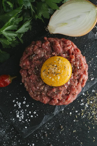 Çiğ biftek. Sığır eti çiğ et baharat, ot ve yumurta sarısı ile kıyılmış. Taze, baharatlı, lezzetli, gurme yemek ile kopya alanı, koyu arka plan üzerinde yakın çekim. Üstten Görünüm.