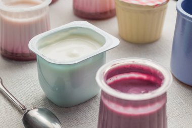 Plastik yoğurt ürün yelpazesine beyaz Tekstil arka plan üzerinde kaseler. Doğal ve sağlıklı meyve, diyet, gurme tatlı granola kahvaltı için. Tatlı yoğurt portre