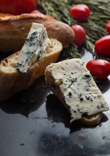 Blue cheese with french baguette, tomato and herbs on black marble table. Traditional snacks in France and Italy — Stock Photo, Image