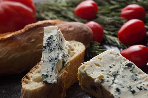 Blue cheese with french baguette, tomato and herbs on black marble table. Traditional snacks in France and Italy — Stock Photo, Image