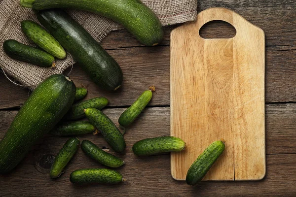 Zucchini and cucumbers on wooden background with kitchen board — Stock Photo, Image