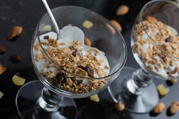 Granola con yogurt, noci e frutta in ciotola di vetro su fondo scuro. Delizioso dolce dolce sano per colazione. Cereali, muesli. Copia spazio, primo piano — Foto Stock