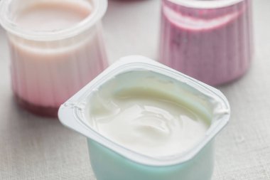 Doğal ve meyve yoğurt çeşitler plastik kase beyaz Tekstil arka plan üzerinde. Sağlıklı, diyet, gurme tatlı granola kahvaltı için. Tatlı yoğurt portre