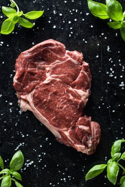 Taze biftek servis ile baharat, domates ve fesleğen mermer zemin üzerine yapraklar. Bir mutfak yemek pişmemiş biftek. Lezzetli, baharatlı, sulu et kopya alanı closeup ile