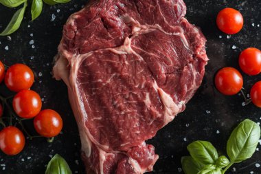 Taze biftek servis ile baharat, domates ve fesleğen mermer zemin üzerine yapraklar. Bir mutfak yemek pişmemiş biftek. Lezzetli, baharatlı, sulu et kopya alanı closeup ile