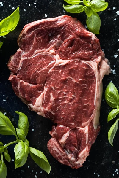Taze biftek servis ile baharat, domates ve fesleğen mermer zemin üzerine yapraklar. Bir mutfak yemek pişmemiş biftek. Lezzetli, baharatlı, sulu et kopya alanı closeup ile