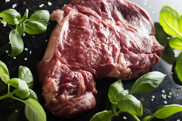 Taze biftek servis ile baharat, domates ve fesleğen mermer zemin üzerine yapraklar. Bir mutfak yemek pişmemiş biftek. Lezzetli, baharatlı, sulu et kopya alanı closeup ile