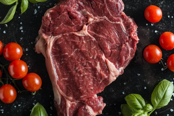Taze biftek servis ile baharat, domates ve fesleğen mermer zemin üzerine yapraklar. Bir mutfak yemek pişmemiş biftek. Lezzetli, baharatlı, sulu et kopya alanı closeup ile