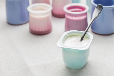 Plastik yoğurt ürün yelpazesine beyaz Tekstil arka plan üzerinde kaseler. Doğal ve sağlıklı meyve, diyet, gurme tatlı granola kahvaltı için. Tatlı yoğurt portre