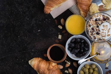 Kahvaltı çeşitli yoğurt, granola, kahve, meyve suyu, kruvasan, zeytin. Meze sabah yemekleri ile karıştırın. Koyu arka plan üzerinde sağlıklı, taze, lezzetli yemek. Üstten Görünüm. Kopya alanı