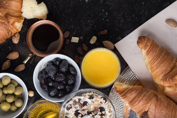 Kahvaltı çeşitli yoğurt, granola, kahve, meyve suyu, kruvasan, zeytin. Meze sabah yemekleri ile karıştırın. Koyu arka plan üzerinde sağlıklı, taze, lezzetli yemek. Üstten Görünüm. Kopya alanı
