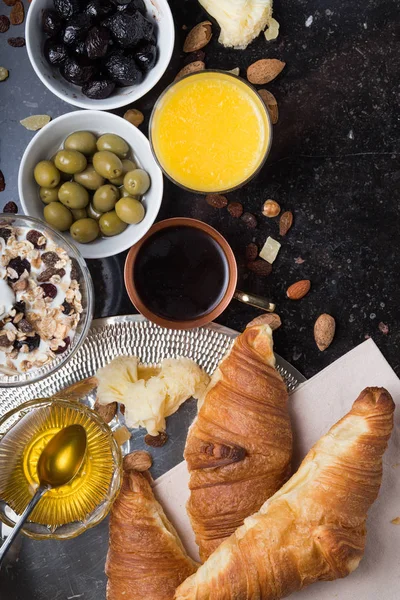 Desayuno surtido de yogur, granola, café, jugo, croissant, aceitunas. Aperitivo mezcla con platos de la mañana. Comida sana, fresca y deliciosa sobre fondo oscuro. Vista superior. Copiar espacio —  Fotos de Stock