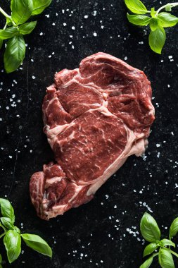 Taze biftek servis ile baharat, domates ve fesleğen mermer zemin üzerine yapraklar. Bir mutfak yemek pişmemiş biftek. Lezzetli, baharatlı, sulu et kopya alanı closeup ile